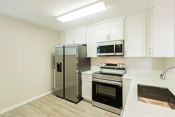 Kitchen with stainless steel appliances, light wood-type flooring, white cabinetry, and light stone countertops