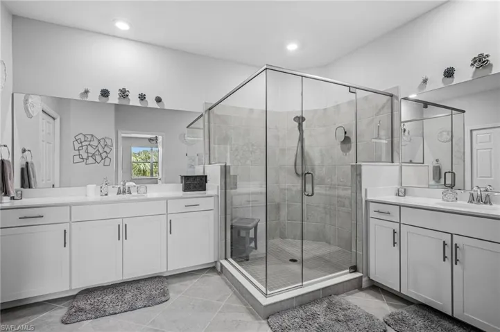 Bathroom featuring two vanities, a shower stall, recessed lighting, and tile patterned floors