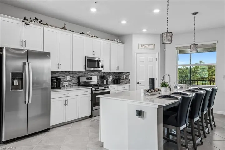 Kitchen featuring appliances with stainless steel finishes, light tile patterned flooring, a kitchen island with sink, recessed lighting, and decorative backsplash