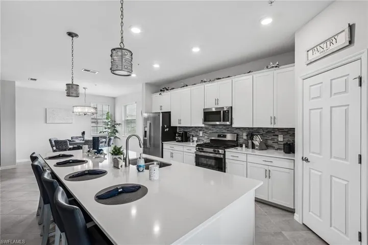 Kitchen featuring appliances with stainless steel finishes, backsplash, an island with sink, recessed lighting, and white cabinets