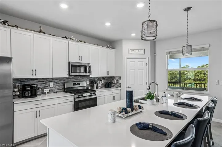 Kitchen with stainless steel appliances, backsplash, light countertops, recessed lighting, and a center island with sink