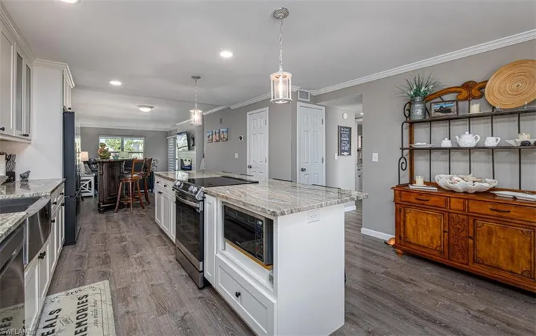 Kitchen featuring a center island, dark hardwood / wood-style floors, light stone counters, white cabinetry, and stainless steel appliances