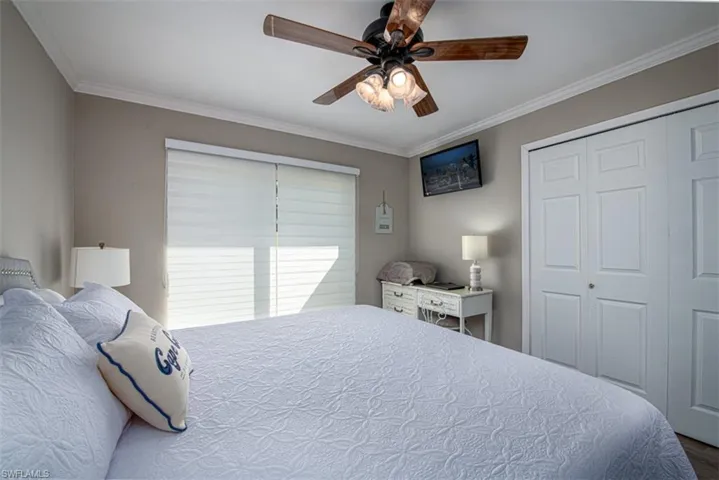 Bedroom with ceiling fan, wood-type flooring, ornamental molding, and a closet