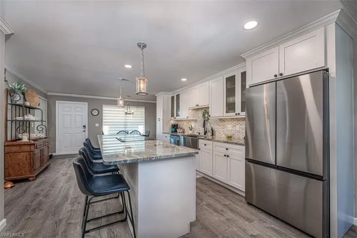 Kitchen with light stone countertops, white cabinetry, stainless steel appliances, and light wood-type flooring