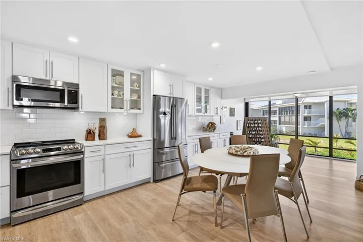 Kitchen featuring appliances with stainless steel finishes, glass insert cabinets, white cabinetry, decorative backsplash, and light wood-type flooring