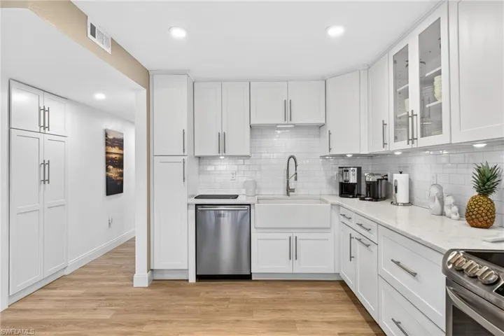 Kitchen featuring stainless steel appliances, white cabinets, glass insert cabinets, light stone countertops, and recessed lighting