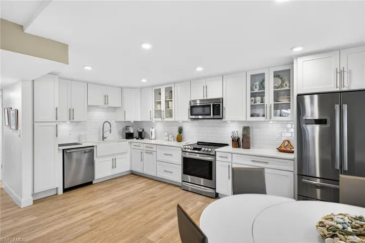Kitchen with appliances with stainless steel finishes, white cabinets, glass insert cabinets, light stone counters, and backsplash