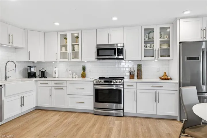Kitchen with appliances with stainless steel finishes, glass insert cabinets, white cabinetry, light stone counters, and recessed lighting