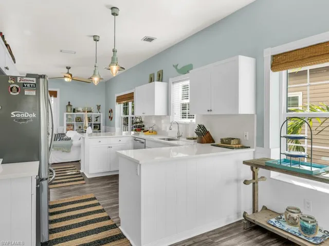 Kitchen featuring white cabinetry, decorative light fixtures, stainless steel refrigerator, sink, and kitchen peninsula