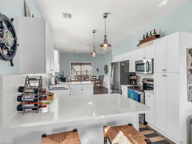 Kitchen with white cabinetry, appliances with stainless steel finishes, a kitchen bar, hanging light fixtures, and kitchen peninsula