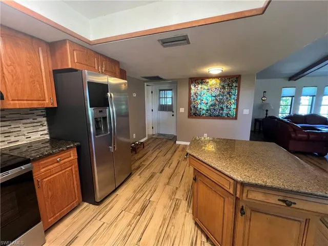 Kitchen with stainless steel appliances, brown cabinets, light wood-type flooring, tasteful backsplash, and beam ceiling