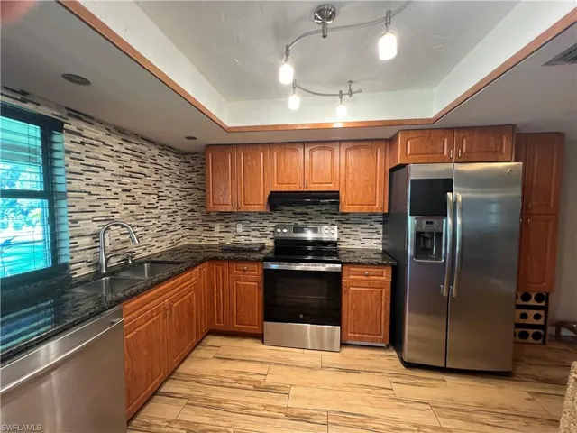 Kitchen with appliances with stainless steel finishes, a tray ceiling, decorative backsplash, and brown cabinetry