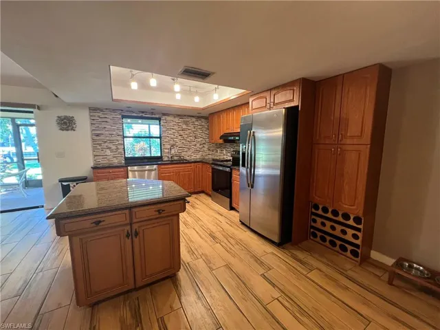 Kitchen with a tray ceiling, appliances with stainless steel finishes, a kitchen island, light wood-style floors, and dark stone counters