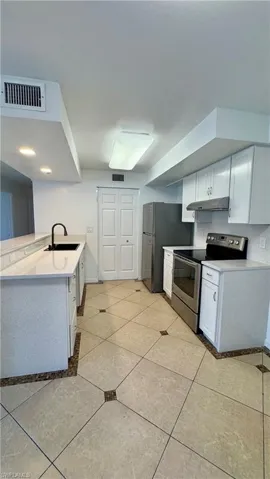 Kitchen featuring light tile patterned floors, stainless steel appliances, white cabinetry, and sink