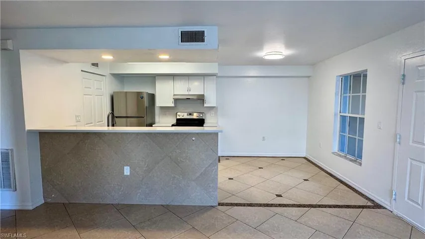 Kitchen featuring kitchen peninsula, white cabinetry, light tile patterned flooring, and stainless steel appliances