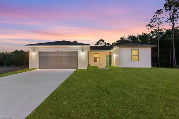 View of front of property featuring concrete driveway, stucco siding, an attached garage, and a lawn