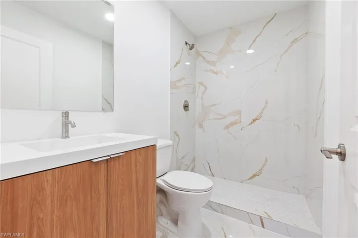 Bathroom with toilet, marble finish floor, vanity, and a marble finish shower