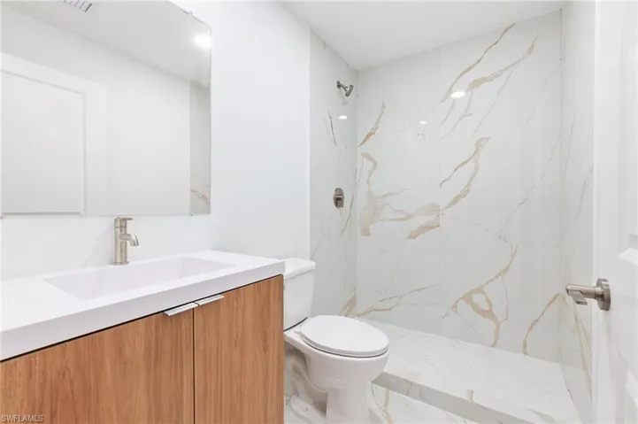 Bathroom featuring toilet, vanity, and a marble finish shower
