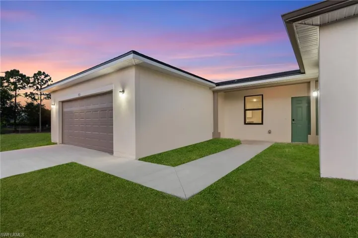 Property exterior at dusk featuring driveway, stucco siding, and a lawn