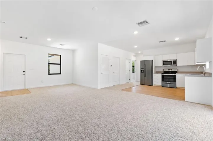 Unfurnished living room featuring light colored carpet, recessed lighting, visible vents, and a sink