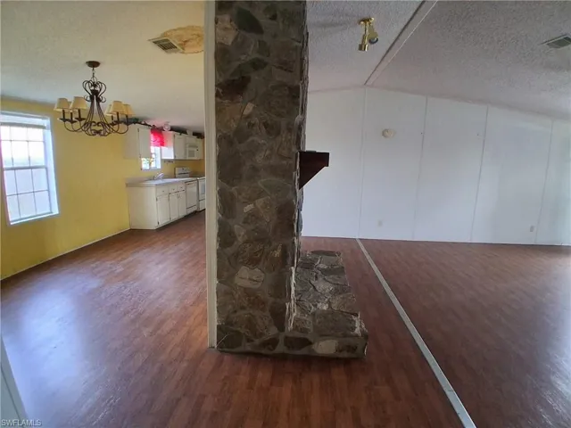 Detailed view of a textured ceiling, wood finished floors, white electric range, suspended lighting, and a decorative wall