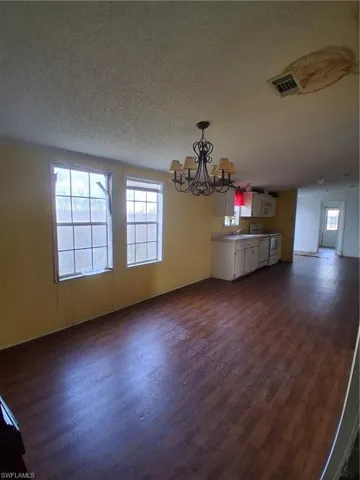 Unfurnished dining area featuring hanging lights, dark wood finished floors, and a textured ceiling