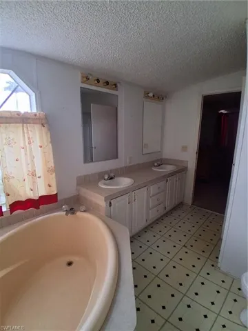Full bathroom featuring double vanity, a textured ceiling, light floors, and a garden tub