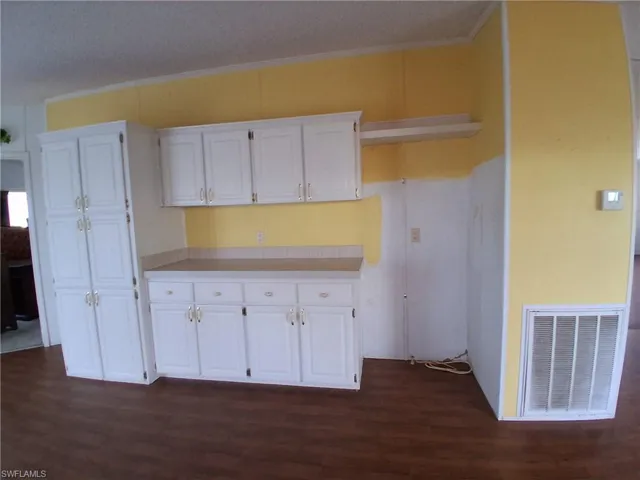 Kitchen with white cabinets, light countertops, dark wood-style flooring, and crown molding