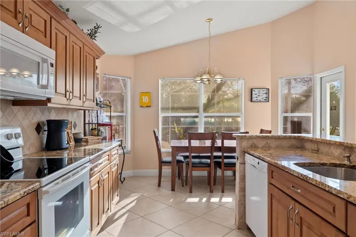 Kitchen with hanging light fixtures, a chandelier, vaulted ceiling, white appliances, and light tile patterned floors