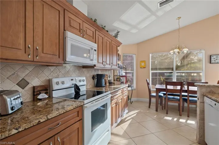 Kitchen with white appliances, lofted ceiling, hanging light fixtures, a notable chandelier, and light tile patterned flooring