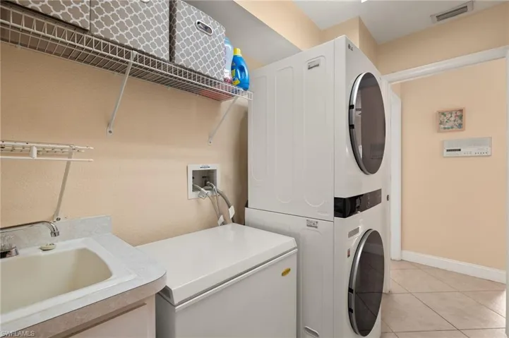 Laundry area with light tile patterned flooring, sink, and stacked washer / dryer