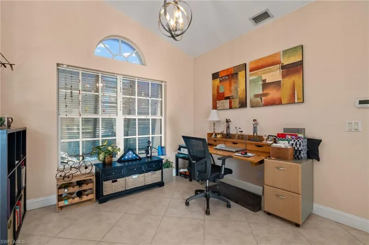 Home office featuring light tile patterned floors, an inviting chandelier, and vaulted ceiling