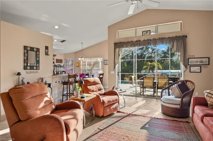 Living room with light tile patterned floors, ceiling fan with notable chandelier, and vaulted ceiling