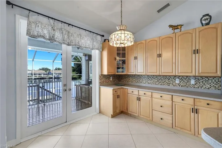 Kitchen with light wood finish cabinets, lofted ceiling, glass fronted cabinets, decorative backsplash, and light countertops