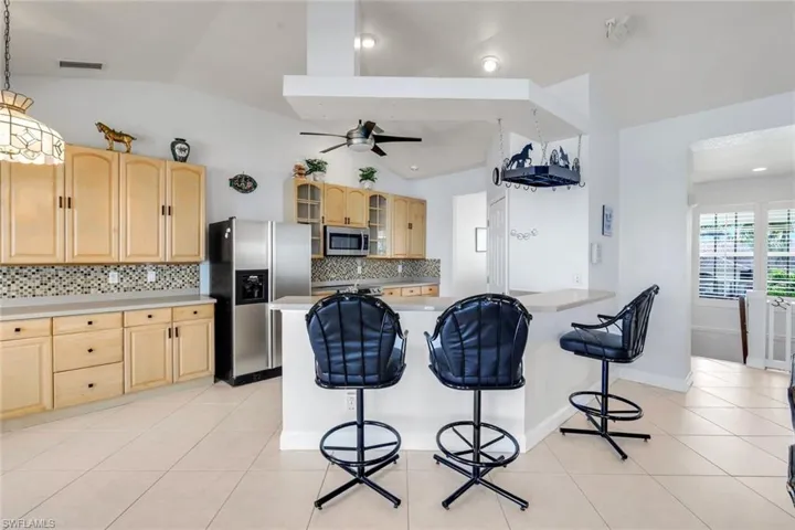 Kitchen featuring glass fronted cabinets, light wood finish cabinets, a kitchen bar, light countertops, and stainless steel appliances