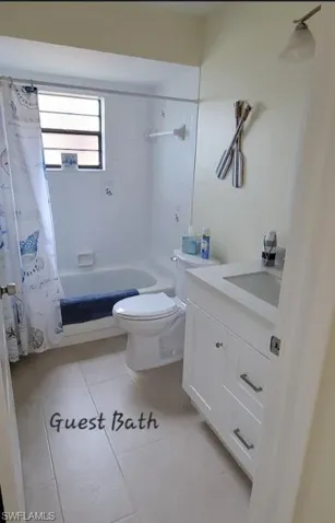 Full bath with tile patterned flooring, shower / bathtub combination with curtain, toilet, and vanity