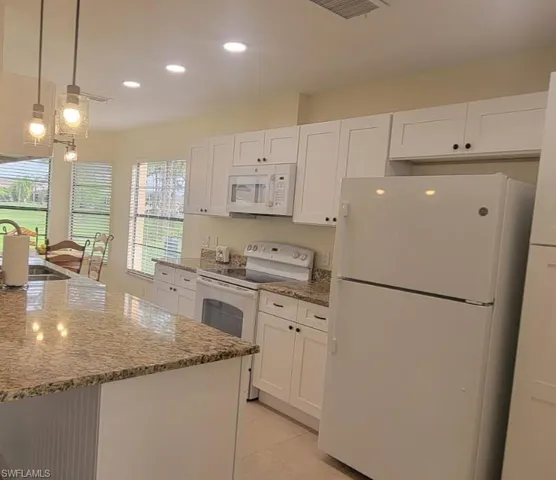 Kitchen featuring white appliances, white cabinets, light stone counters, and a sink