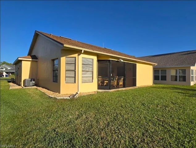 Rear view of house with cooling unit, a lawn, a sunroom, and stucco siding