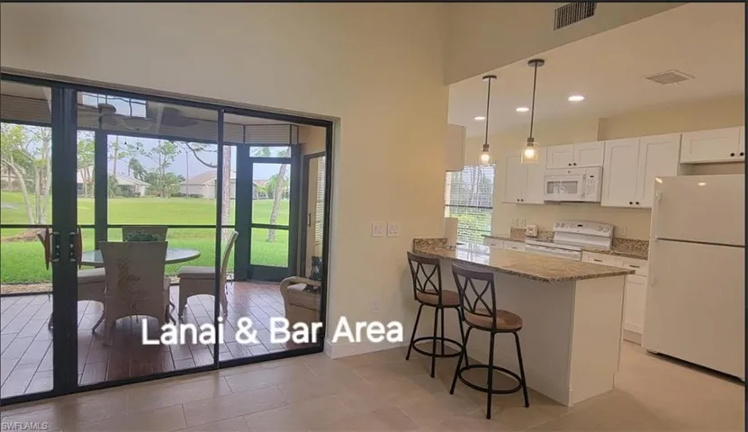 Kitchen with visible vents, a kitchen bar, white cabinetry, white appliances, and light stone countertops