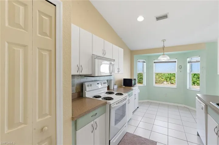 Kitchen with white appliances, white cabinetry, lofted ceiling, decorative light fixtures, and light tile patterned floors