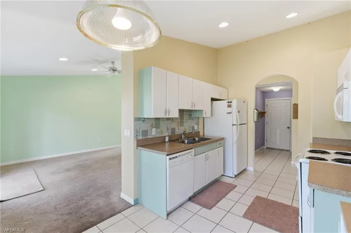 Kitchen featuring arched walkways, white appliances, white cabinetry, light tile patterned floors, and tasteful backsplash