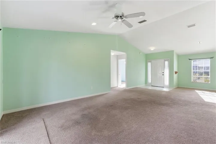 Unfurnished living room with ceiling fan, vaulted ceiling, and carpet flooring