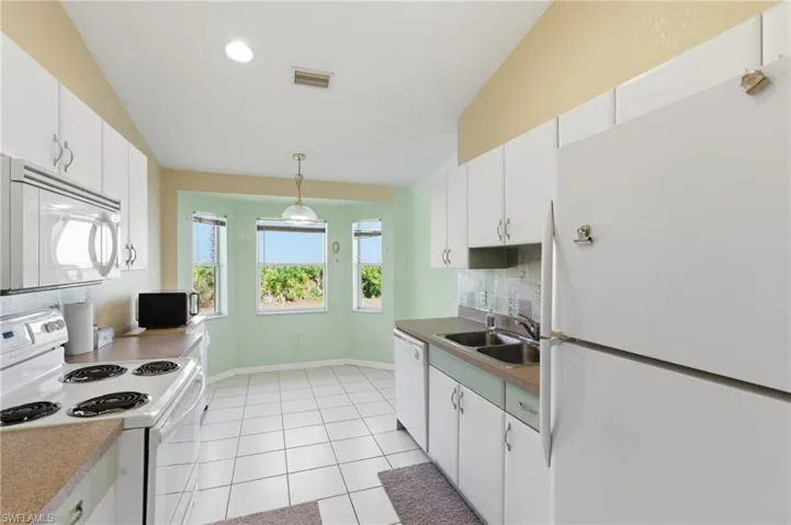 Kitchen featuring white appliances, white cabinetry, decorative light fixtures, tasteful backsplash, and vaulted ceiling