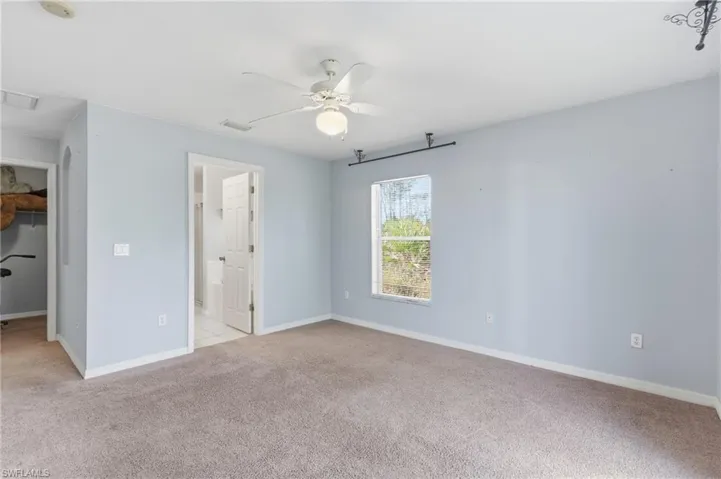 Unfurnished bedroom with light colored carpet, a spacious closet, ceiling fan, and ensuite bath