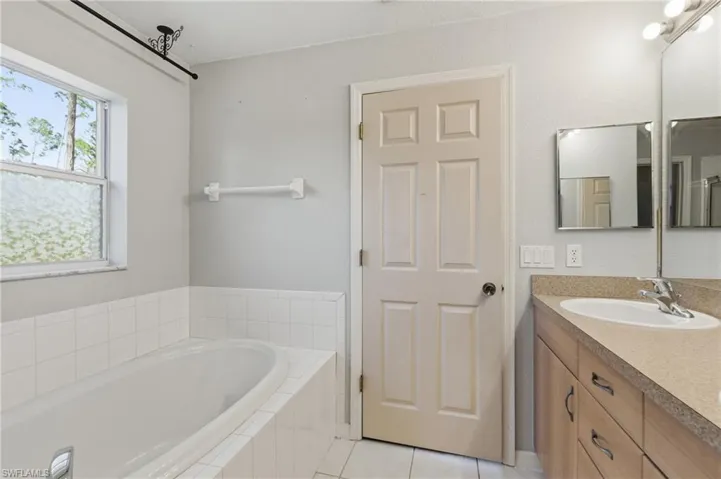 Bathroom with vanity, a garden tub, and light tile patterned floors