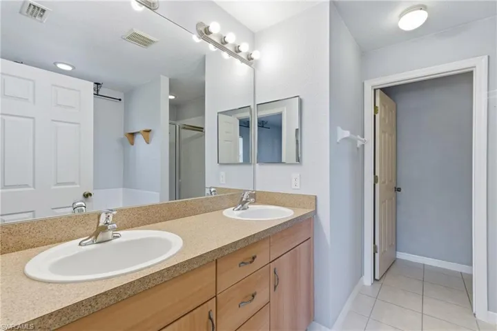 Full bath featuring double vanity, a shower stall, and light tile patterned flooring
