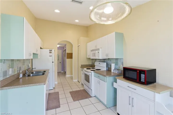 Kitchen featuring white appliances, backsplash, arched walkways, white cabinetry, and light tile patterned floors
