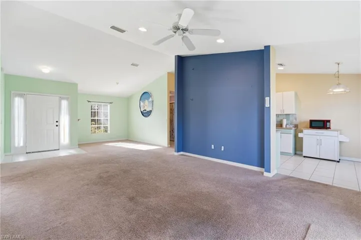 Unfurnished living room featuring lofted ceiling, light carpet, a ceiling fan, and light tile patterned floors