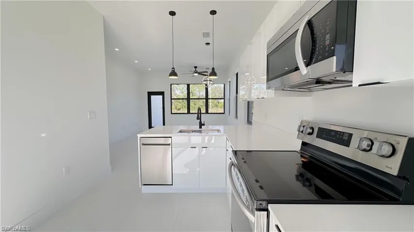 Kitchen with stainless steel appliances, a peninsula, white cabinets, decorative light fixtures, and light tile patterned flooring