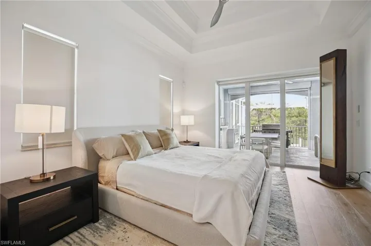 Primary bedroom on ground floor with slider access to lanai light wood floors, raised tray ceiling, and ornamental molding